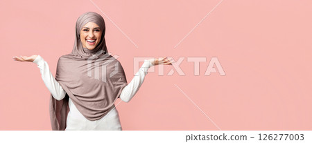 Cheerful muslim girl in hijab demonstrating something on her empty palms, comparing variants, making scales of her hands over pink background Cheerful muslim girl in hijab demonstrating something on her empty palms, comparing variants, making scales of her hands over pink background 126277003