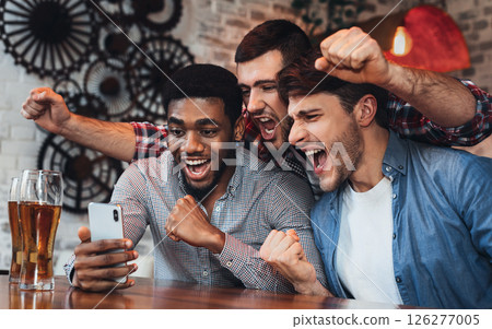 Men watching football on smartphone and drinking beer in bar Men watching football on smartphone and drinking beer in bar 126277005