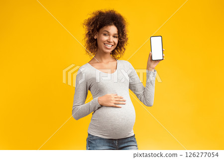 Cool app. Happy pregnant woman showing phone with blank screen over pink background 126277054