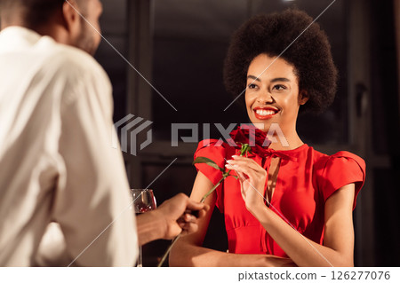 Romantic Date. Afro Man Giving Girlfriend Red Rose Flower Dining Celebrating Anniversary Or Valentine's Day Sitting In Restaurant In Evening 126277076