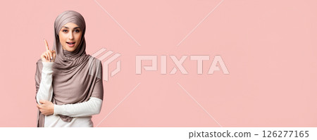 I have idea. Smart muslim girl in hijab pointing finger up, found problem solution, posing over pink background, panorama with empty space 126277165