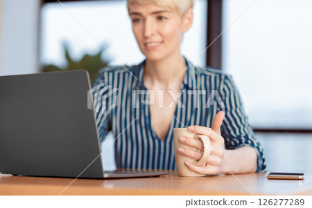 Mature Lady At Laptop Working On Business Report Holding Coffee Cup Sitting In Modern Office. Shallow Depth, Selective Focus Mature Lady At Laptop Working On Business Report Holding Coffee Cup Sitting In Modern Office. Shallow Depth, Selective Focus 126277289