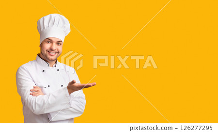 Restaurant Chef. Professional Cook Man Gesturing With Hand Showing Something Standing Over Yellow Studio Background. Panorama With Free Space Restaurant Chef. Professional Cook Man Gesturing With Hand Showing Something Standing Over Yellow Studio Background. Panorama With Free Space 126277295
