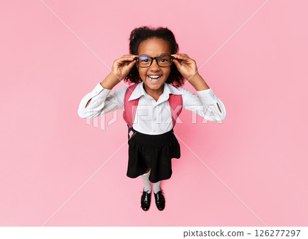 Funny African Schoolgirl Looking At Camera Through Eyeglasses Happy About Back To School Standing On Yellow Studio Background. High-Angle Shot 126277297