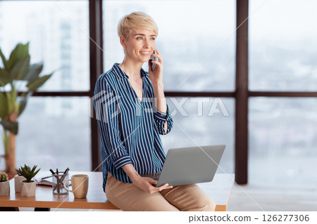 Entrepreneur Woman Talking On Cellphone Sitting With Laptop On Desk In Modern Office. Business Communication Entrepreneur Woman Talking On Cellphone Sitting With Laptop On Desk In Modern Office. Business Communication 126277306