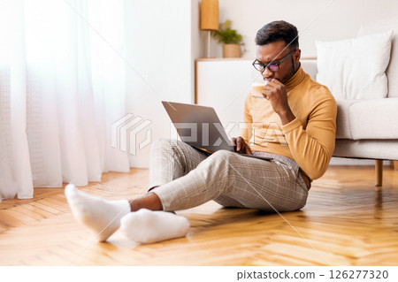 Busy Afro Freelancer Guy Using Laptop Computer Working On Weekend And Having Coffee Sitting On Floor Indoor. Selective Focus Busy Afro Freelancer Guy Using Laptop Computer Working On Weekend And Having Coffee Sitting On Floor Indoor. Selective Focus 126277320