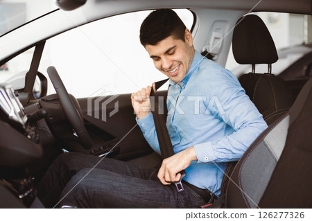 Driving Regulations. Guy Putting On Seat Belt Sitting In New Car In Dealership Center. Selective Focus Driving Regulations. Guy Putting On Seat Belt Sitting In New Car In Dealership Center. Selective Focus 126277326