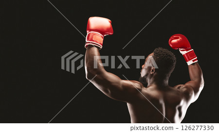 A boxer wearing red gloves raises his arms in victory against a black background. 126277330