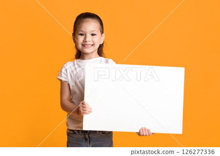 Advertisement Concept. Portrait of smiling asian girl holding empty blank board isolated on yellow studio background. Happy kid standing with white square paper placard for ad, showing it to camera 126277336