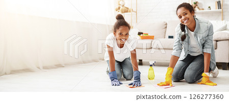 Two adorable african girls cleaning carpet at home, helping parents to keep house tidy, copy space 126277360