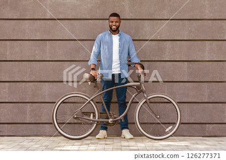 Full length portrait of happy african american man with bicycle standing against grey urban wall and smiling, copy space 126277371