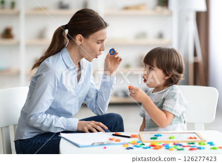 Female speech therapist curing child's problems and impediments. Little boy learning letter O with private English language tutor during lesson at office Female speech therapist curing child's problems and impediments. Little boy learning letter O with private English language tutor during lesson at office 126277423