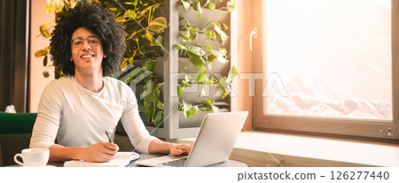 African American young guy wearing eyeglasses sitting at cafe, using laptop and taking notes, working on project or studying online, copy space African American young guy wearing eyeglasses sitting at cafe, using laptop and taking notes, working on project or studying online, copy space 126277440