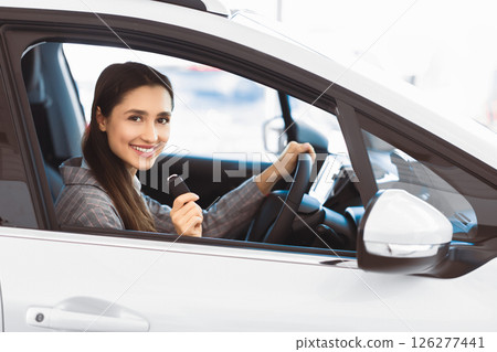 Joyful Woman Showing Car Key Smiling To Camera Sitting In Driver's Seat In New Automobile Dealership Store Joyful Woman Showing Car Key Smiling To Camera Sitting In Driver's Seat In New Automobile Dealership Store 126277441