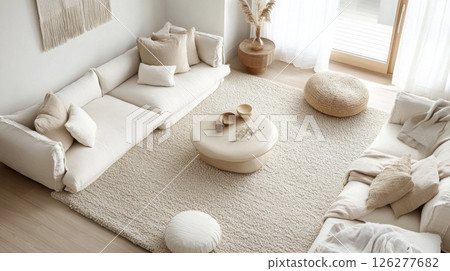 The image shows a living room with a white sofa, a white rug, and a round white coffee table with wooden bowls. The room is also decorated with throw pillows, a woven footstool, and a potted plant. 126277682