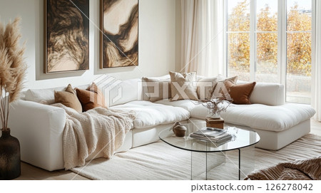 A cozy living area features a large white sectional sofa adorned with soft cushions and a warm throw. The room is bathed in natural light, highlighting abstract art and seasonal decorations. 126278042