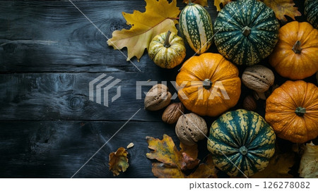 Various pumpkins and walnuts are artistically arranged among autumn leaves on a rustic wooden table. 126278082