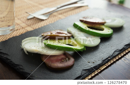 Chopped vegetables black tomatoes, avocado and onions against black stone board Chopped vegetables black tomatoes, avocado and onions against black stone board 126278470