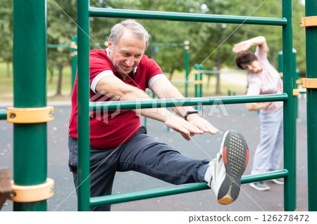 Elderly man doing stretching exercises on a sports bar at an outdoor sports ground Elderly man doing stretching exercises on a sports bar at an outdoor sports ground 126278472