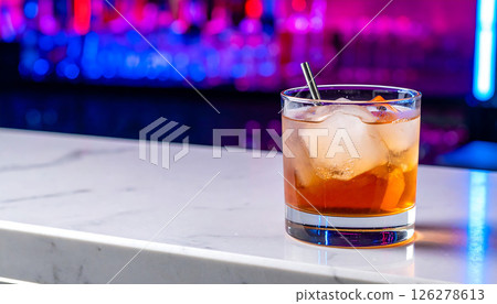 A close-up of an amber-colored cocktail with ice and orange garnish on a bar counter, with blurred colorful lights in the background. A close-up of an amber-colored cocktail with ice and orange garnish on a bar counter, with blurred colorful lights in the background. 126278613