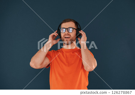 Listening and enjoying the music. In headphones. Handsome man is in the studio against blue background 126278867