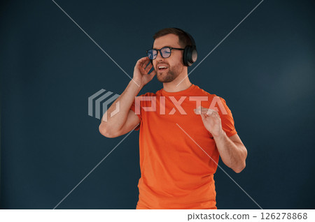 Listening and enjoying the music. In headphones. Handsome man is in the studio against blue background 126278868
