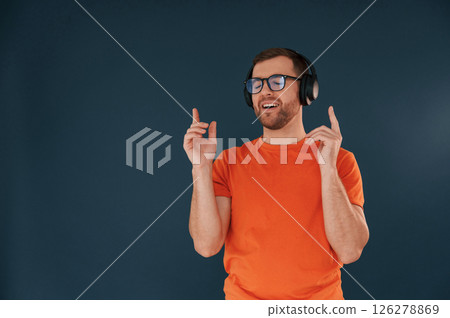 Listening and enjoying the music. In headphones. Handsome man is in the studio against blue background Listening and enjoying the music. In headphones. Handsome man is in the studio against blue background 126278869