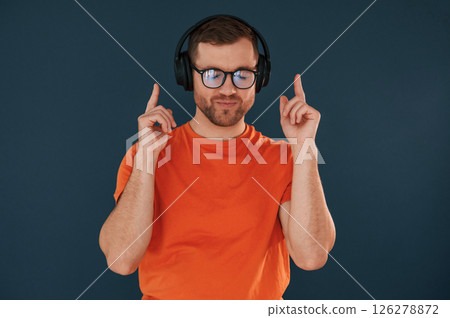 Listening and enjoying the music. In headphones. Handsome man is in the studio against blue background 126278872
