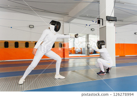 Two female fencers competing in bright indoor fencing hall. Two female fencers competing in bright indoor fencing hall. 126278994