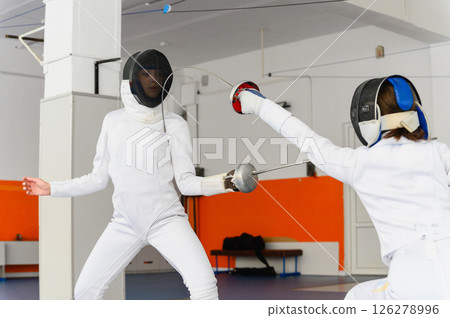 Female fencer lunging forward to strike opponent indoors. Female fencer lunging forward to strike opponent indoors. 126278996
