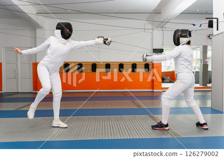 Female fencer leaping forward in attack during indoor match. Female fencer leaping forward in attack during indoor match. 126279002