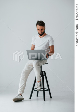 On the chair with laptop. Handsome man is in the studio against white background 126279034