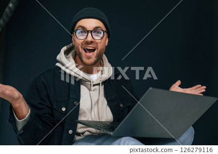 Celebrating success. Feeling uplifting. Using laptop. Handsome man is in the studio against background Celebrating success. Feeling uplifting. Using laptop. Handsome man is in the studio against background 126279116