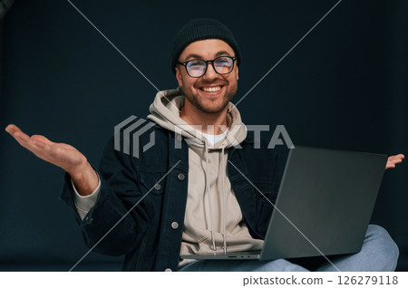 Smiling, sitting and using laptop. Handsome man is in the studio against background 126279118