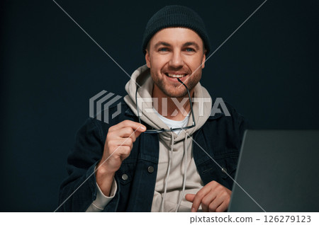 Smiling and sitting by laptop. Handsome man is in the studio against background 126279123