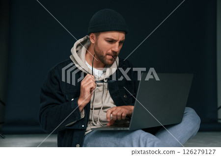 Sitting and using laptop. Handsome man is in the studio against background 126279127