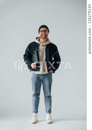 IT specialist in hat and glasses standing with laptop. Handsome man is in the studio against white background IT specialist in hat and glasses standing with laptop. Handsome man is in the studio against white background 126279134