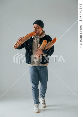 Guy is walking and holding baguettes. Handsome man is in the studio against white background 126279171