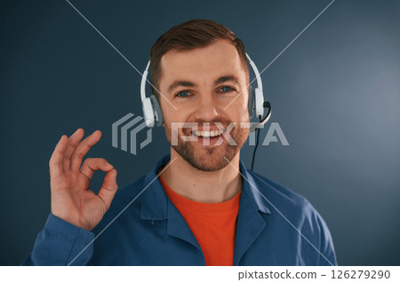 Showing fine, okay, good, sign. Smiling. In headphones. Handsome man is in the studio against blue background 126279290