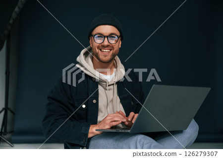 Using laptop and smiling. Handsome man is in the studio against background Using laptop and smiling. Handsome man is in the studio against background 126279307
