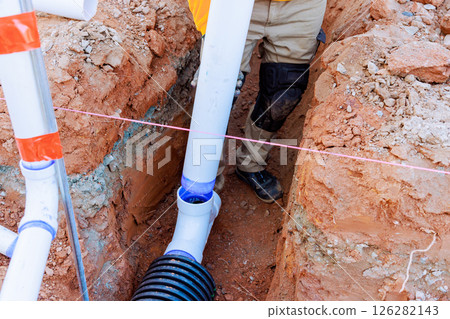 Construction workers set up drainage pipes in trench, ensuring proper installation alignment. Construction workers set up drainage pipes in trench, ensuring proper installation alignment. 126282143