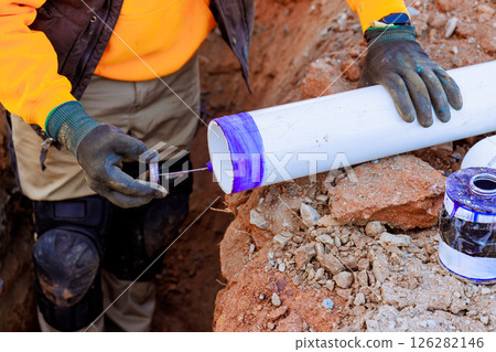 Construction worker is using blue adhesive on white PVC pipe on set up drainage pipe system in trench Construction worker is using blue adhesive on white PVC pipe on set up drainage pipe system in trench 126282146