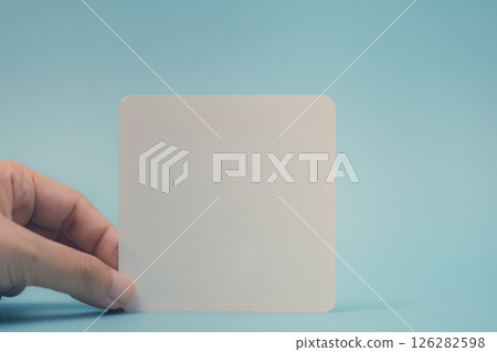 Female Hand Holding a Blank White Note Against a Blue Background 126282598