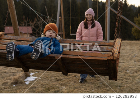 A boy swings on a swing with his mother. A boy swings on a swing with his mother. 126282958