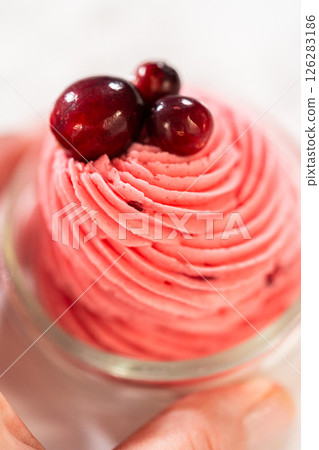 A swirl of vibrant cranberry buttercream piped into a glass jar and topped with fresh cranberries. This creamy, tart frosting is perfect for cookies, cakes, and holiday desserts. 126283186