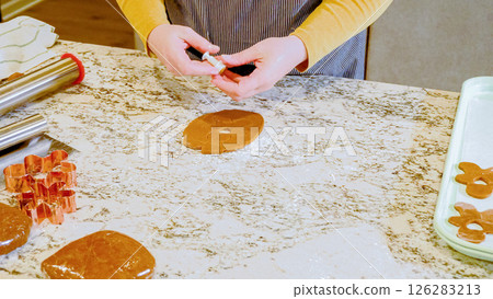 Using various festive cookie cutters, we're cutting out charming gingerbread cookies from the rolled dough on the sleek marble counter, bringing holiday cheer to the modern kitchen. 126283213