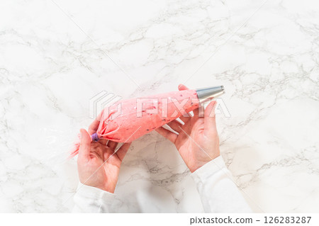 A piping bag filled with vibrant cranberry buttercream, ready for decorating lemon spritz cookies. The smooth buttercream is prepared for precise and beautiful decoration with a star tip nozzle. A piping bag filled with vibrant cranberry buttercream, ready for decorating lemon spritz cookies. The smooth buttercream is prepared for precise and beautiful decoration with a star tip nozzle. 126283287