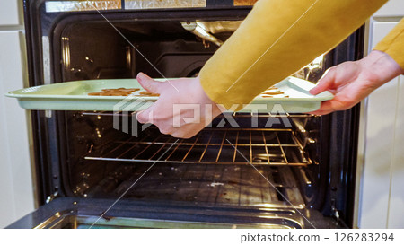 Scrumptious gingerbread cookies getting baked to perfection in a gas oven, filling the kitchen with warm, aromatic holiday bliss. 126283294