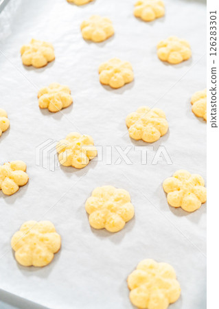 Golden lemon spritz cookies rest on a sheet of parchment paper, showcasing their delicate floral shape and light, crisp texture. These buttery cookies are infused with bright citrus flavor, making Golden lemon spritz cookies rest on a sheet of parchment paper, showcasing their delicate floral shape and light, crisp texture. These buttery cookies are infused with bright citrus flavor, making 126283301