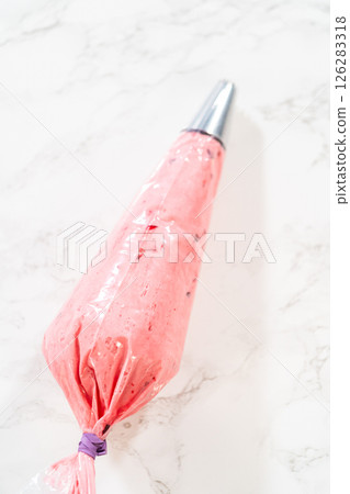 A piping bag filled with smooth cranberry buttercream, ready for decorating cookies or cakes. The frosting has a creamy texture with visible cranberry pieces for a festive touch. A piping bag filled with smooth cranberry buttercream, ready for decorating cookies or cakes. The frosting has a creamy texture with visible cranberry pieces for a festive touch. 126283318